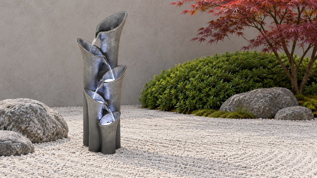 Tall grey leaning petal column fountain with water stepping down the folds, on raked gravel beside smooth boulders