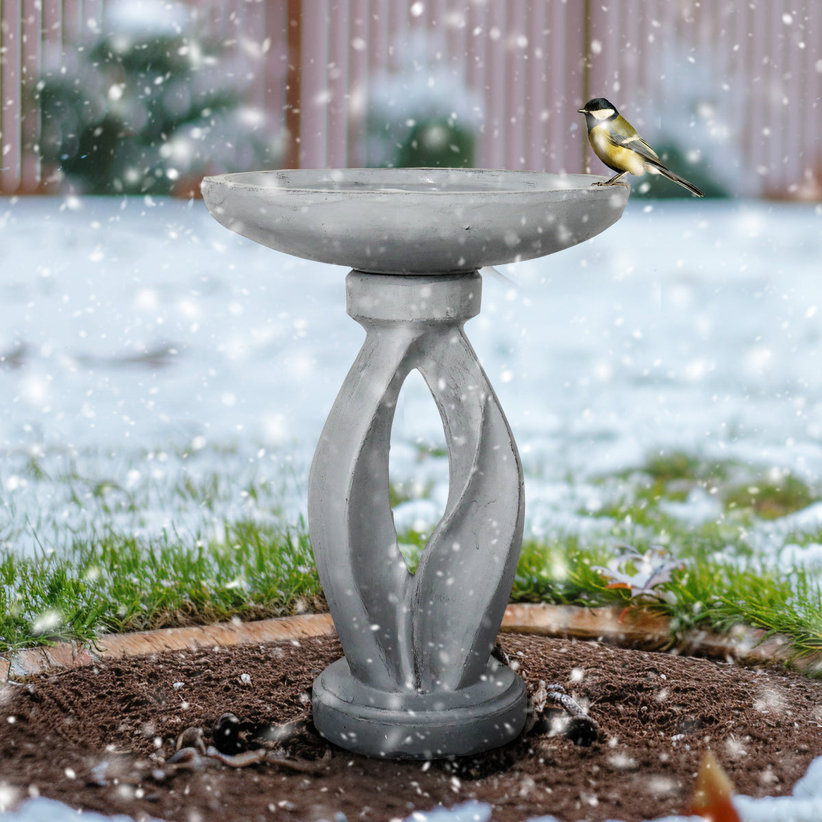 Weather-resistant 13.5kg modern concrete bird bath withstanding snow in a winter garden landscape.