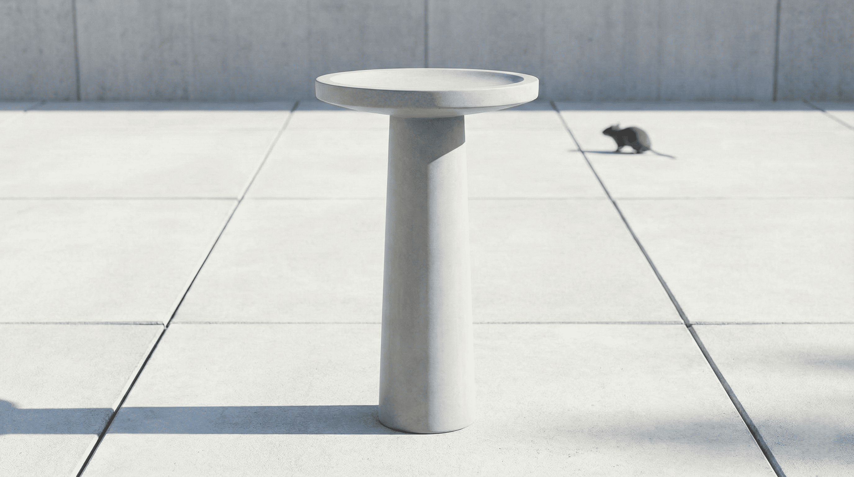 A tall, smooth concrete pedestal bird bath on a clean patio, designed to deter rats and rodents.
