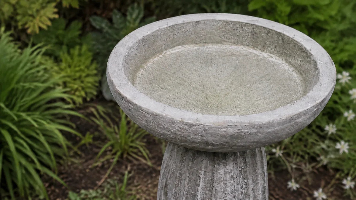 A dry fluted concrete bird bath basin showing its porous surface with mineral crust and staining