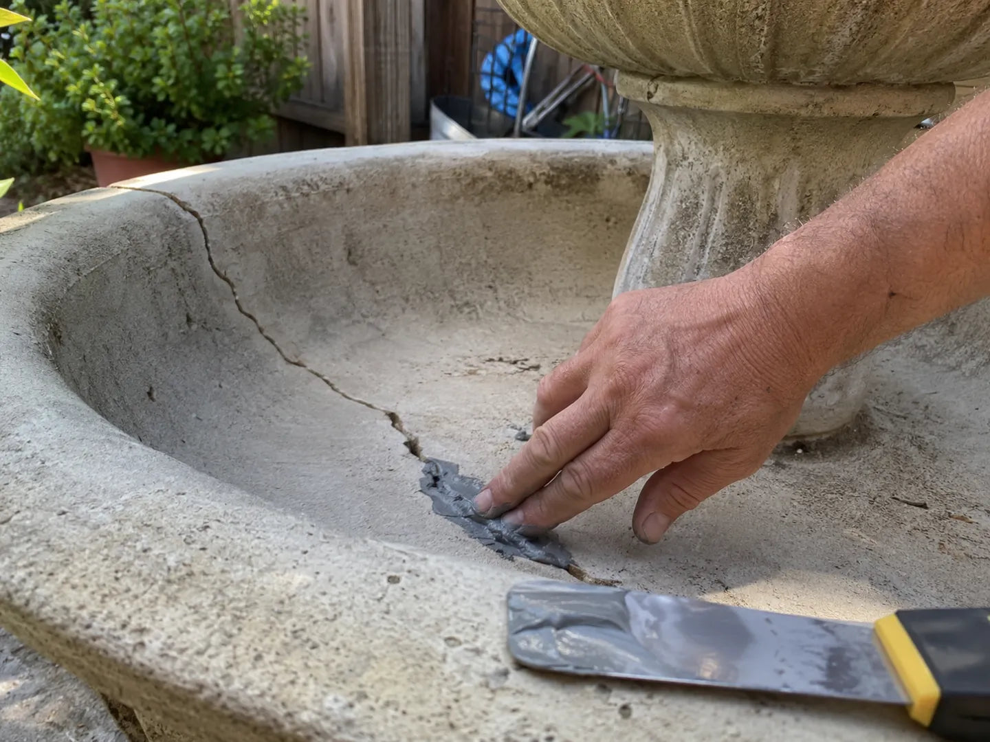 Hand applying patch into a crack on a drained concrete garden fountain