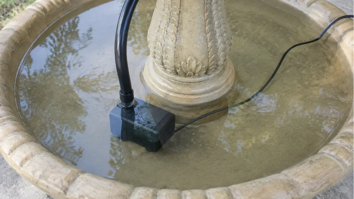 A submersible pump on the floor of a three tier concrete fountain basin with its outlet tube running up