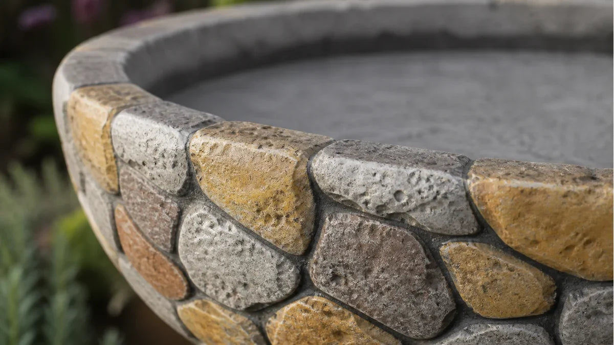 A concrete bird bath basin with real stone pieces inlaid into the surface shown in close detail