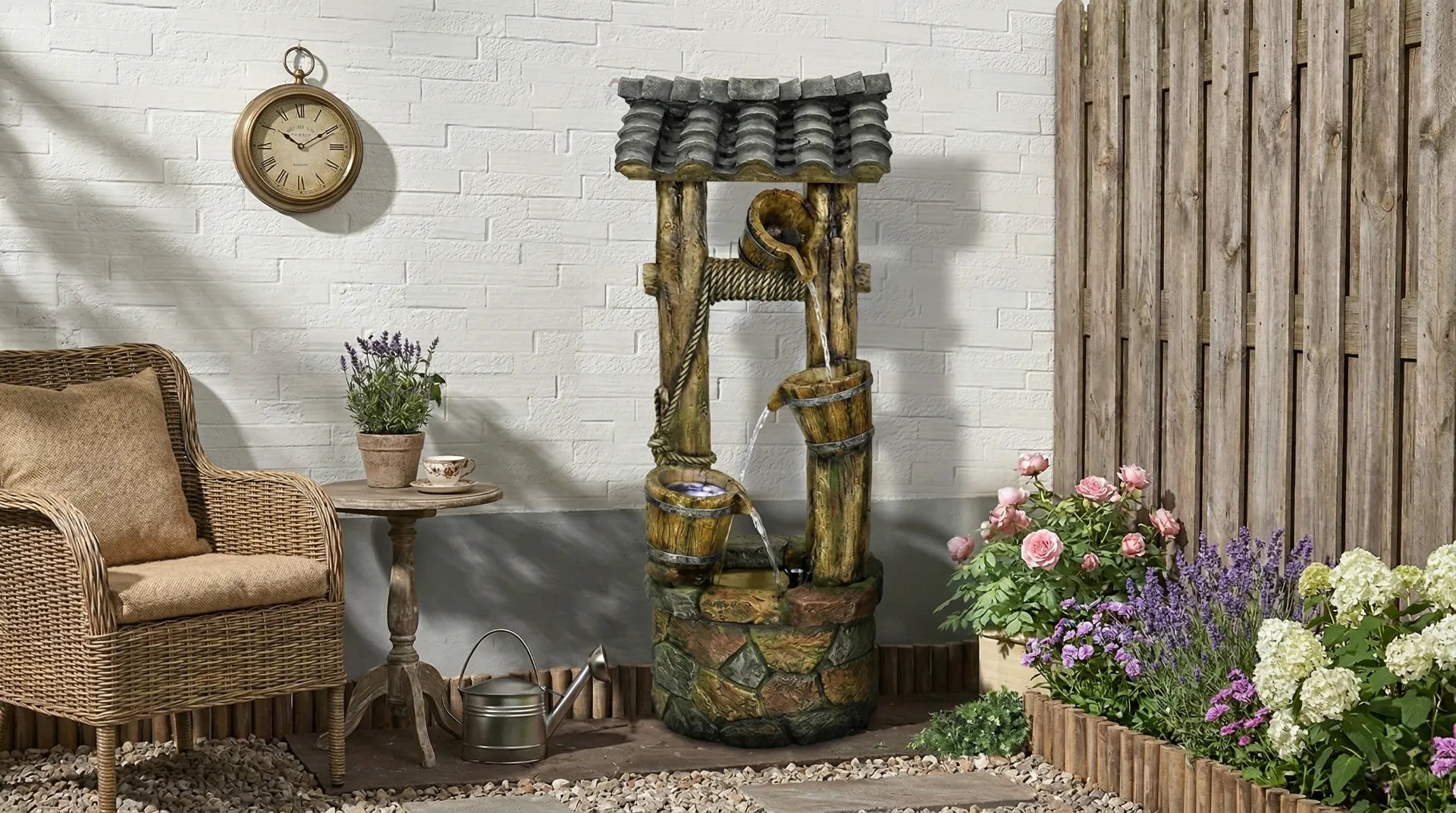 Peaceful garden corner featuring a rustic tiered wooden bucket fountain with integrated LED lights, surrounded by comfortable wicker chairs and blooming flower beds.