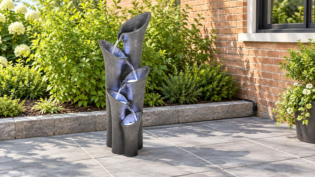 Angled column fountain running on gray paving beside a stone edged planting bed