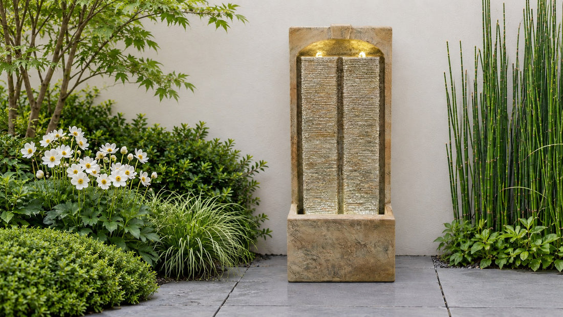 Pale sandstone wall fountain with water sheeting down two tall channels, flanked by white anemones and horsetail
