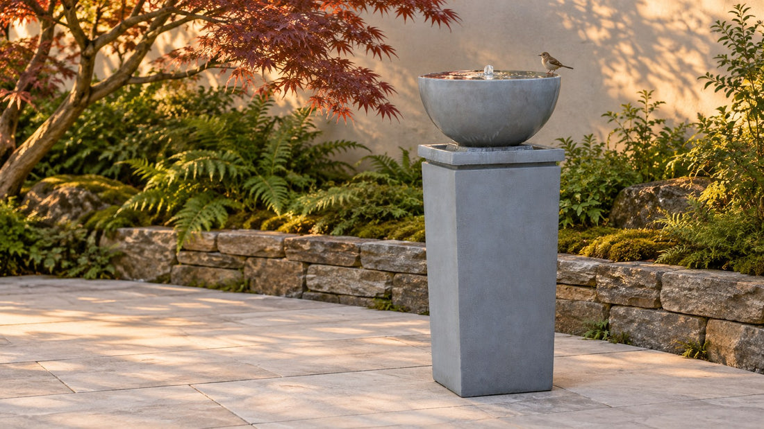 Wide shallow grey bowl on a tall square plinth holding still water, a small bird standing on the rim