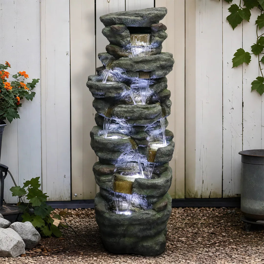 51-inch tall multi-tier rock cascading fountain against a white wooden garden fence.