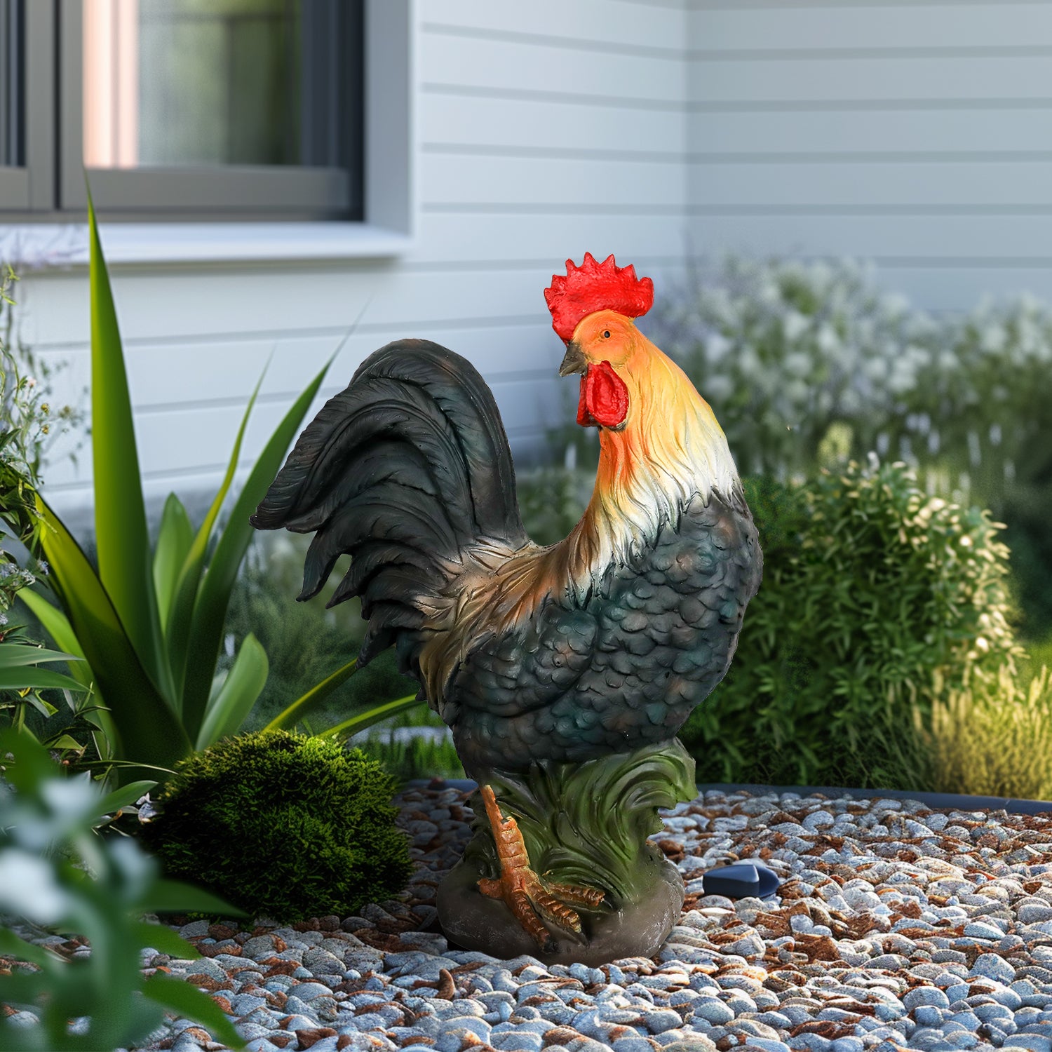A standing, realistic rooster sculpture with vivid red comb and orange neck feathers, placed in a gravel garden.