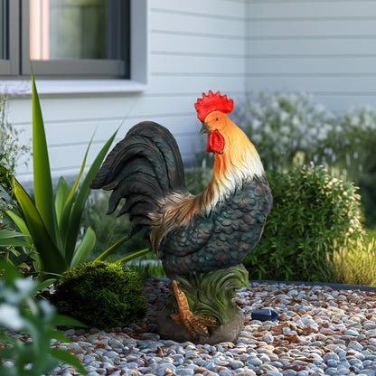 A standing, realistic rooster sculpture with vivid red comb and orange neck feathers, placed in a gravel garden.