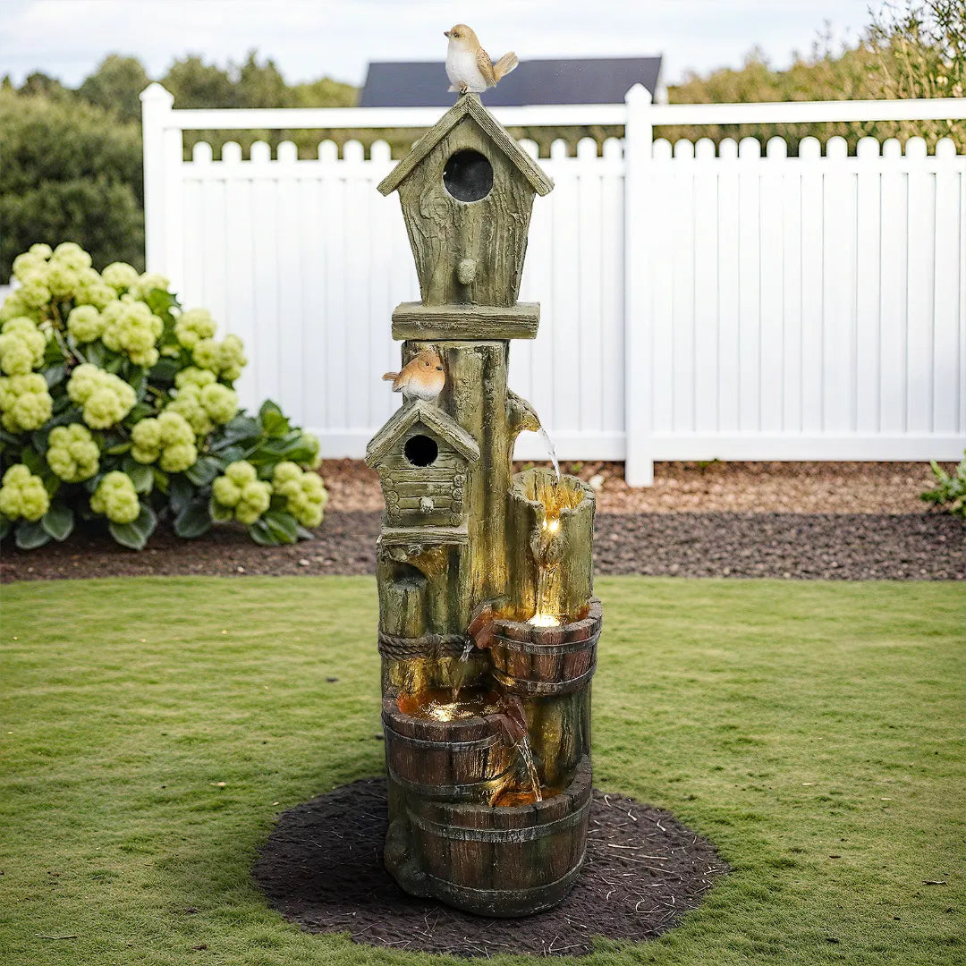 Close-up_of_the_rustic_birdhouse_fountain_with_decorative_songbirds_in_a_lush_green_garden.