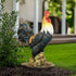 Colorful 22.4-inch rooster garden statue standing in a garden bed with green plants.