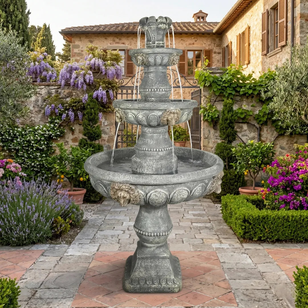 Detailed multi-tiered weathered stone fountain with sculpted lion heads in a lush Mediterranean garden courtyard.