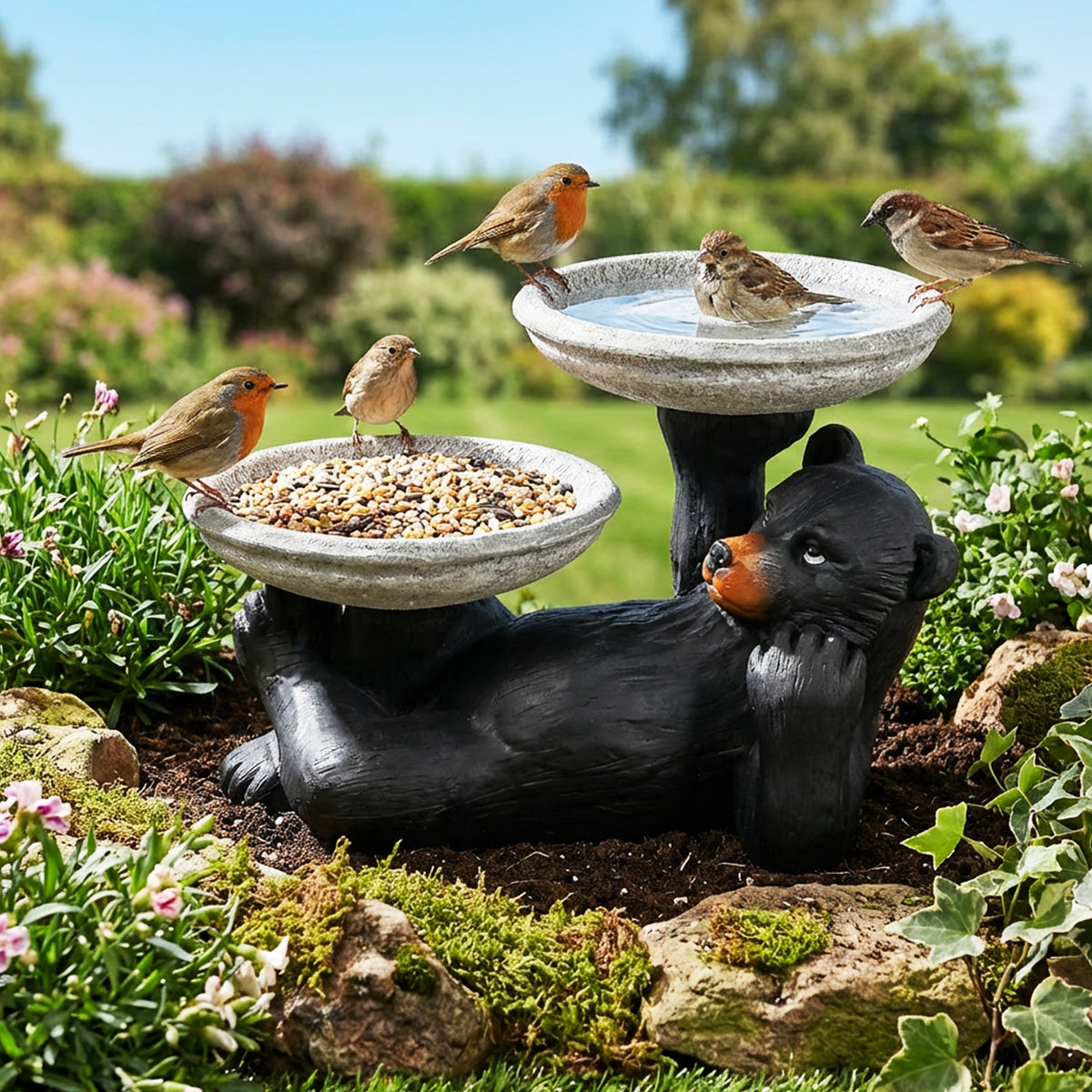 Double bowl black bear statue used as both a bird bath and feeder in a lush backyard.