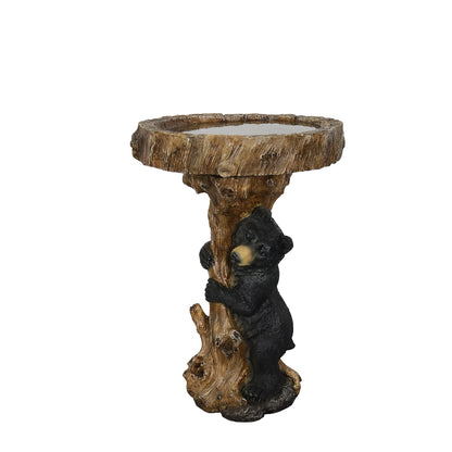 Full view of the black bear hugging a tree stump bird bath on a white background.