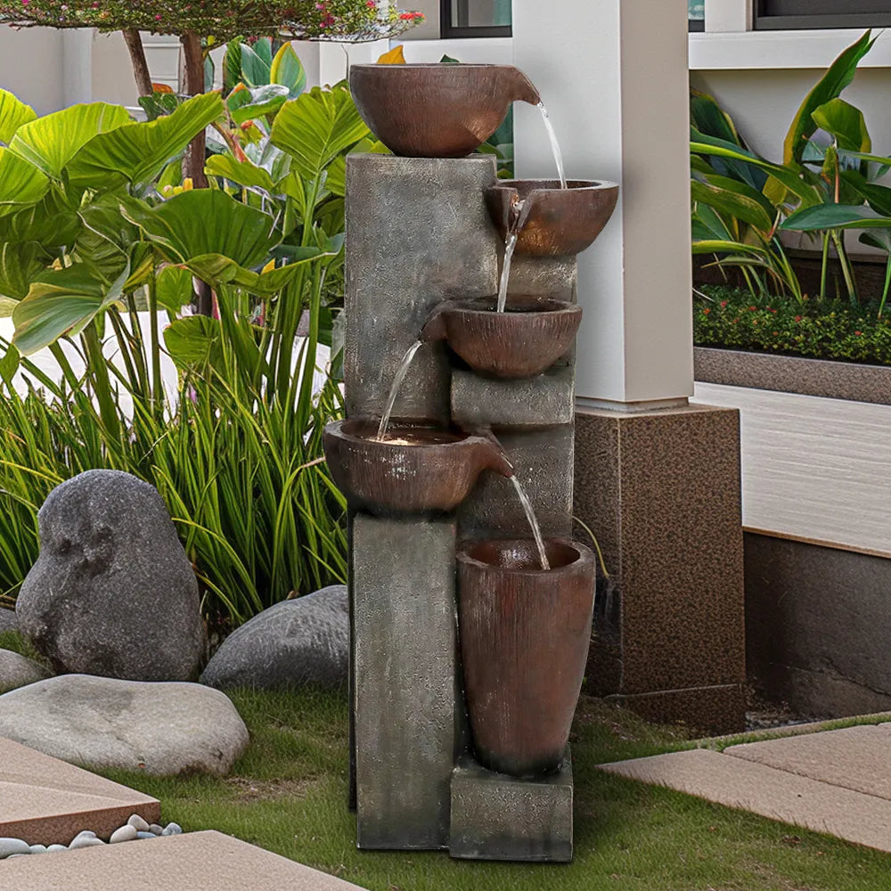 Large outdoor tiered fountain placed against a concrete wall base, showing the vertical water flow.