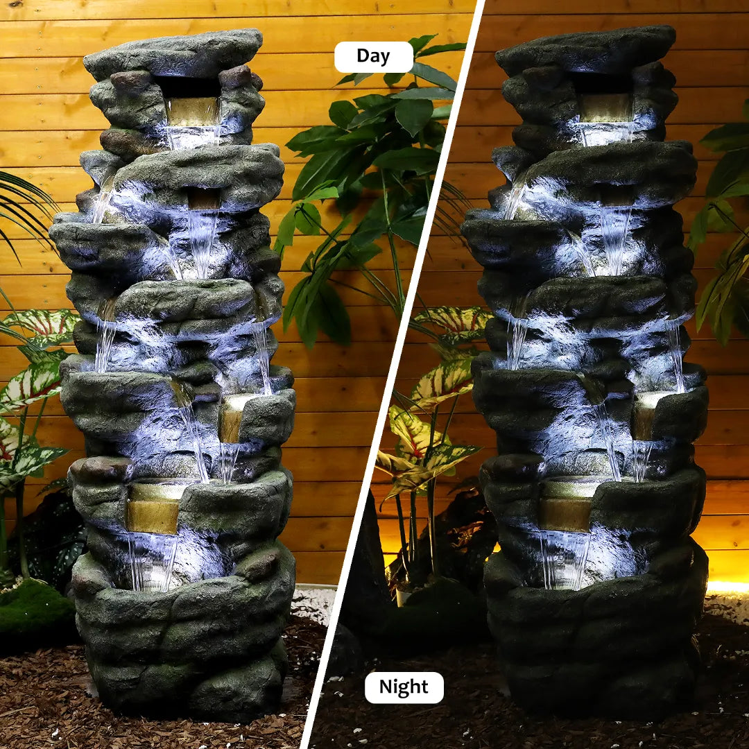 Large rock waterfall fountain with 7 white LED lights illuminating a relaxing backyard patio at night