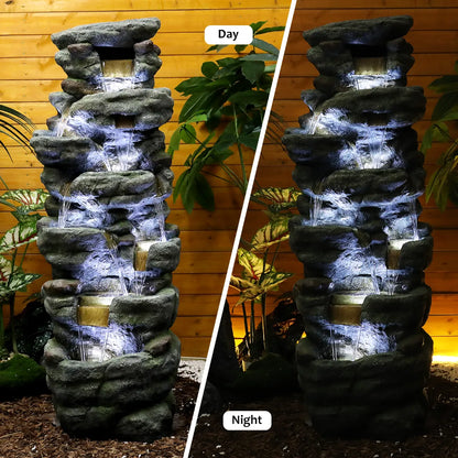 Large rock waterfall fountain with 7 white LED lights illuminating a relaxing backyard patio at night