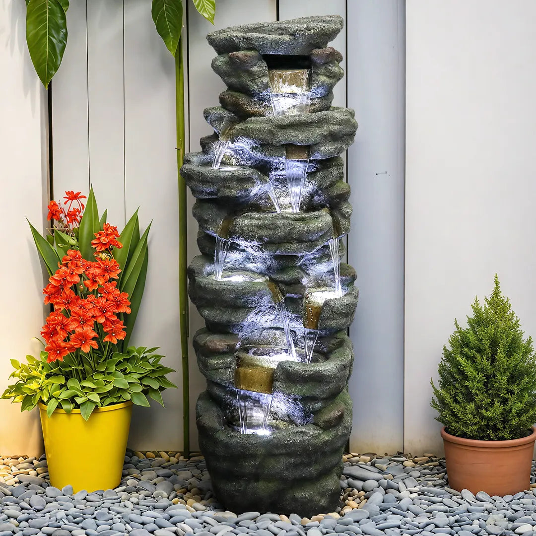 Layered rock water feature positioned naturally next to a rustic outdoor garden fence