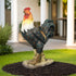 Lifelike rooster garden statue with a red comb and hand-painted feathers in a garden bed.