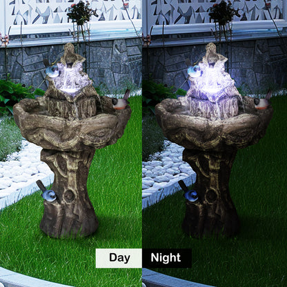 Lighted outdoor bird bath fountain glowing at night in a garden flower bed.