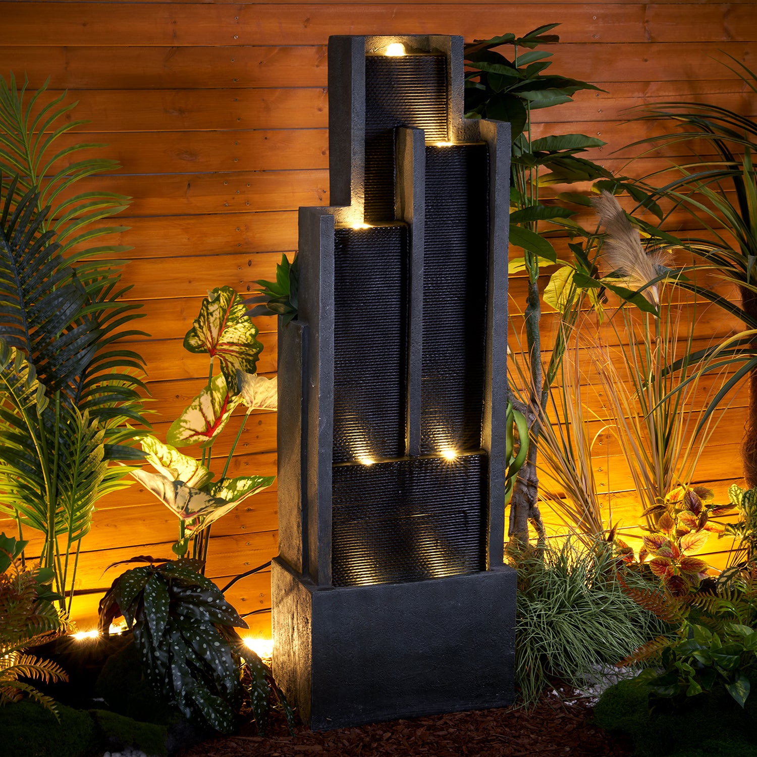 Nighttime view of the modern 4-tier outdoor fountain with magical LED illumination in a garden.