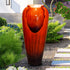 Striking red concrete vase fountain along a peaceful garden pathway