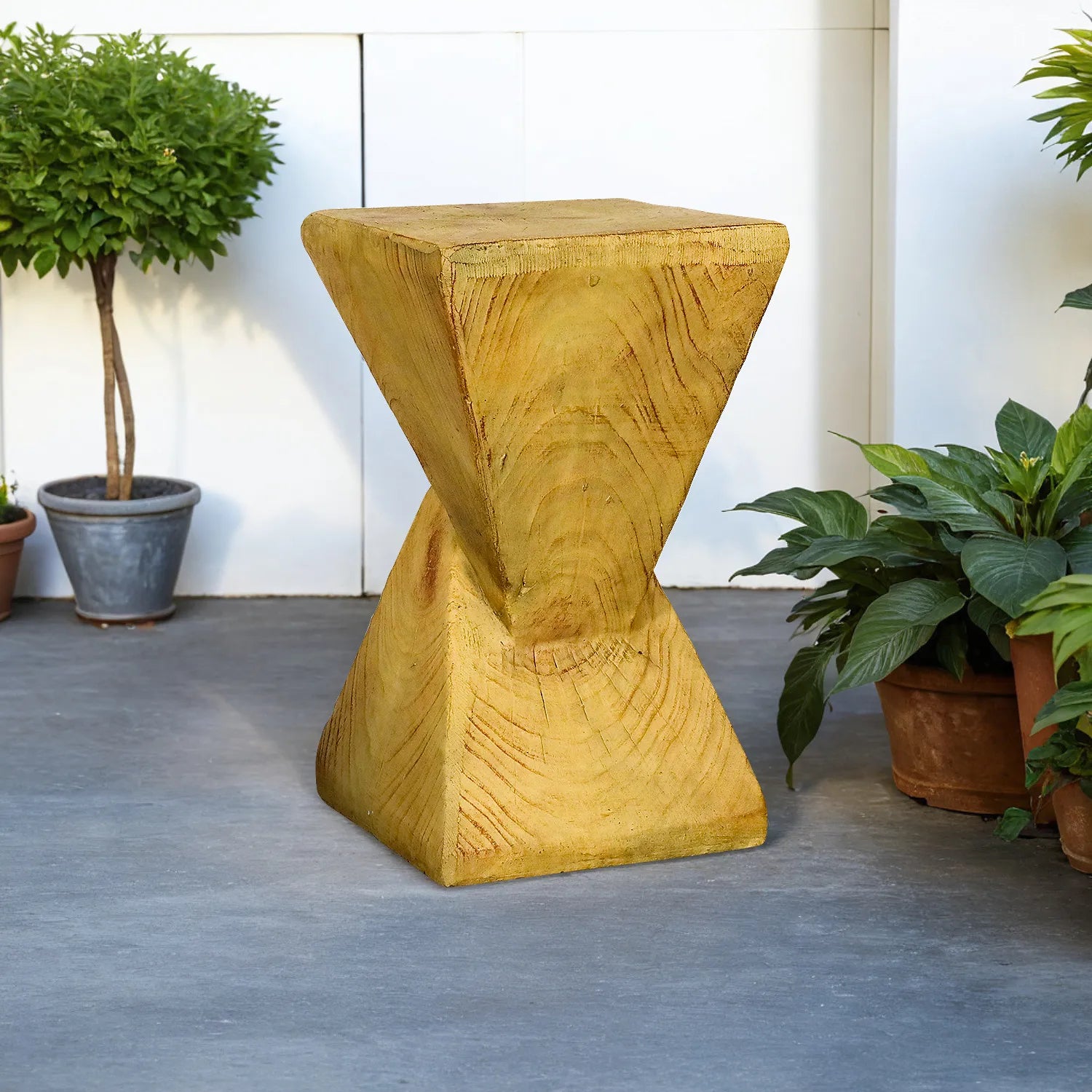Stylish yellow concrete side table placed on a modern outdoor patio next to green plants.