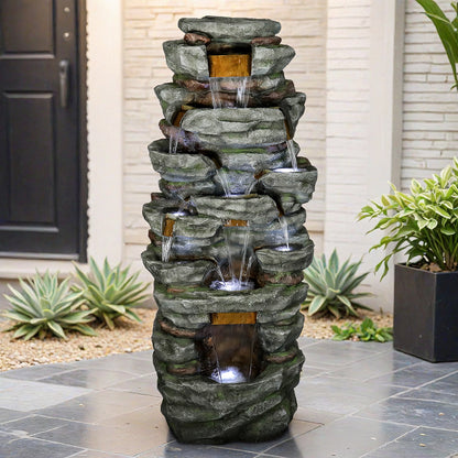 Tall natural stone outdoor fountain next to a wooden garden fence