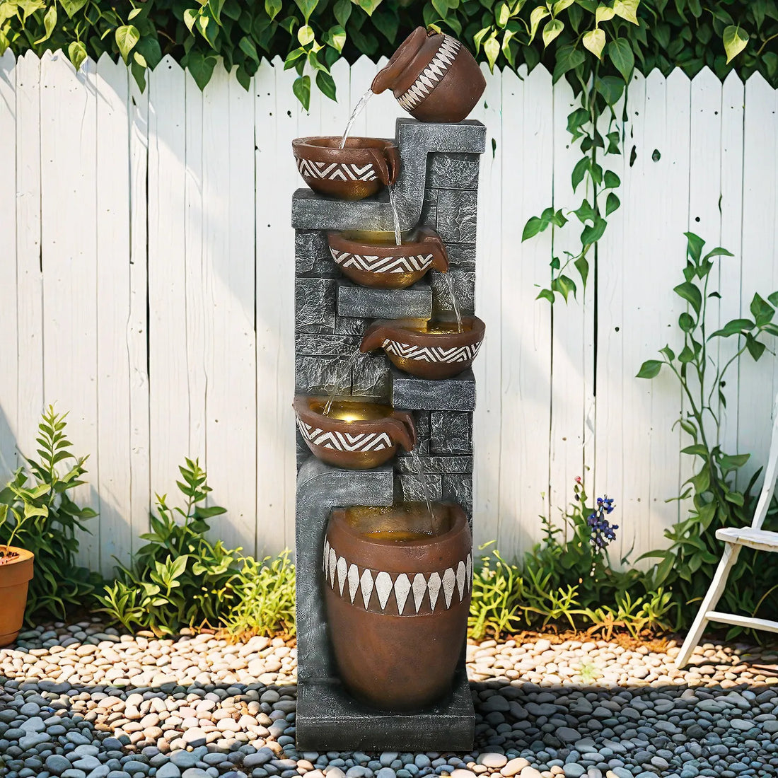 Tallfreestandingpottery-inspiredwaterfountainagainstawhiteoutdoorfence.
