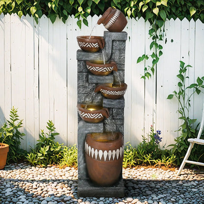 Tallfreestandingpottery-inspiredwaterfountainagainstawhiteoutdoorfence.