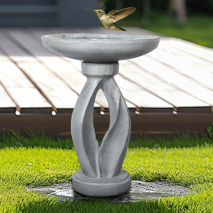 Wild bird flying towards the sleek contemporary geometrical pedestal birdbath on a wooden deck.