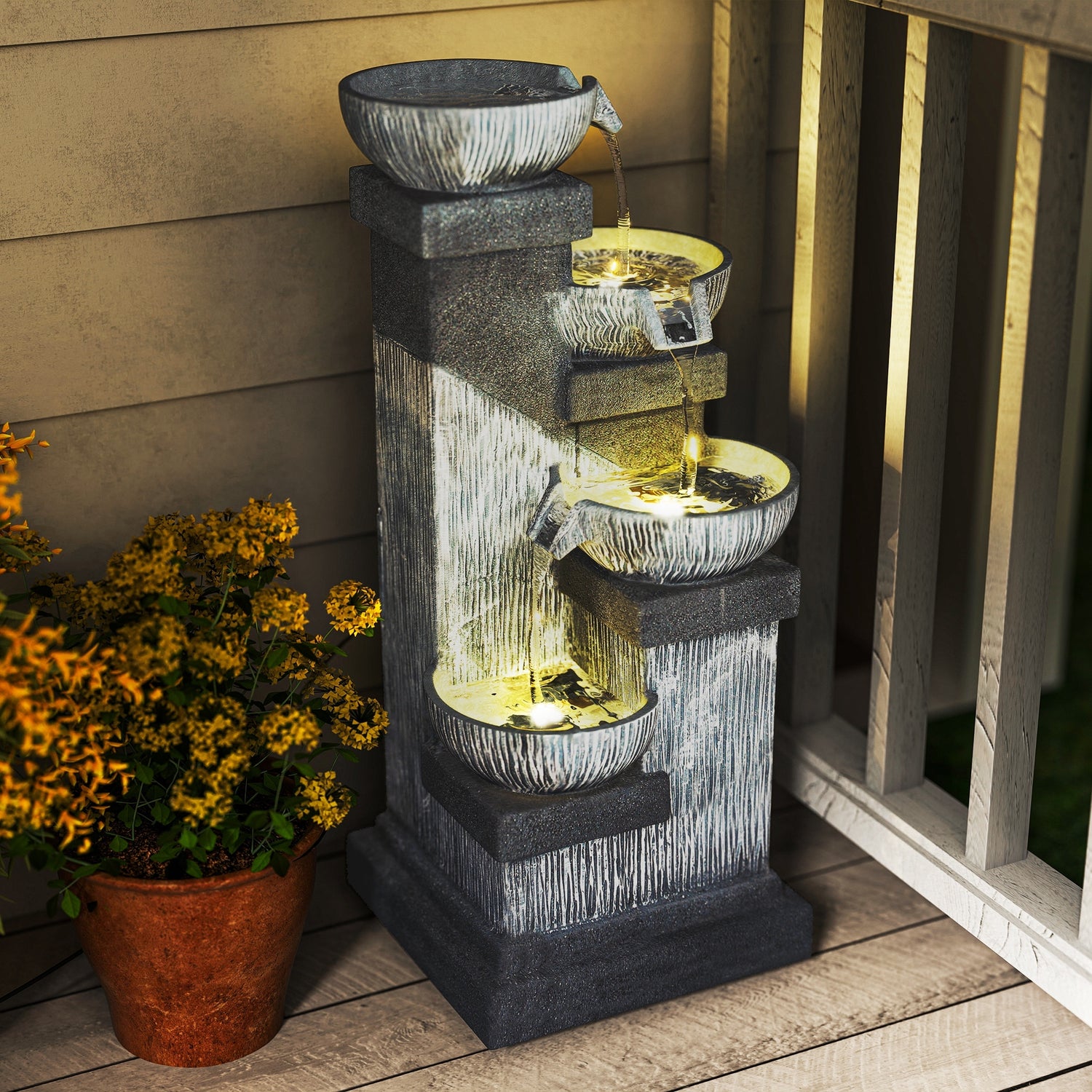 charcoal bowl tower fountain lit warm on a porch beside terracotta pot of orange flowers