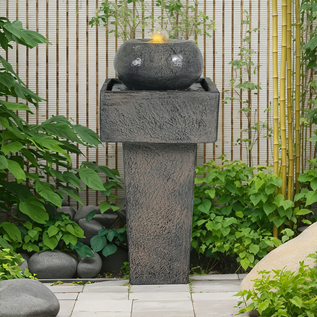 concrete orb column fountain in a zen garden with bamboo fence and river stones