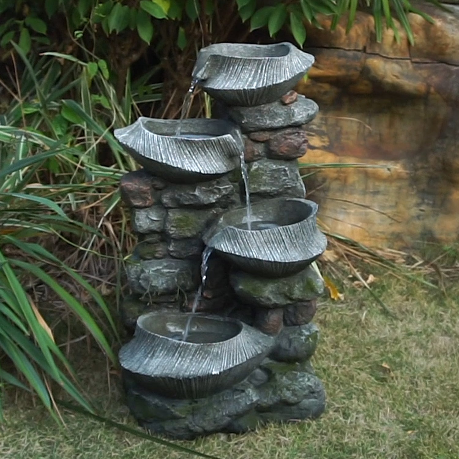 fluted basin rock fountain in a garden beside a stone wall with ferns