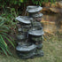 fluted basin rock fountain in a garden beside a stone wall with ferns