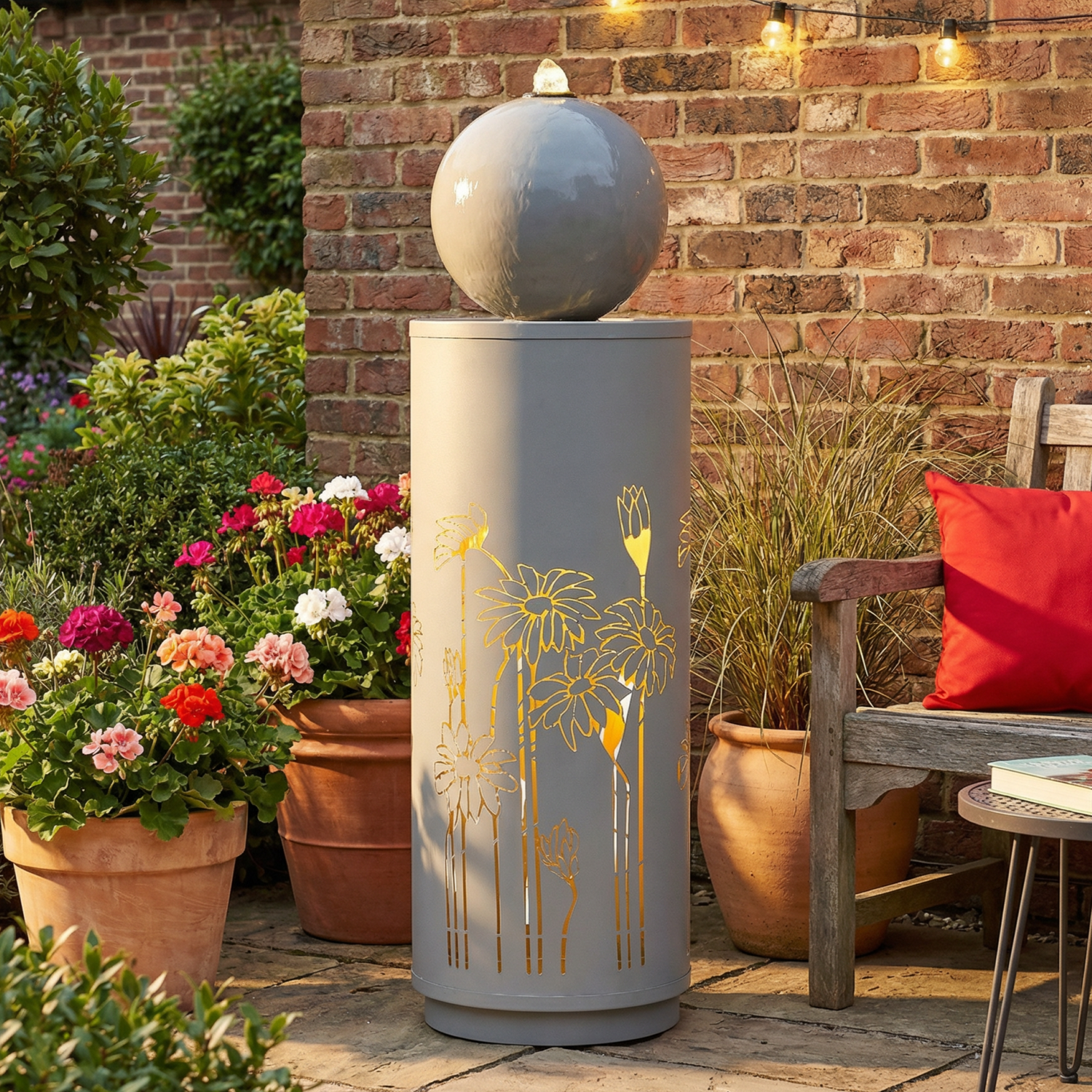 gilded vine cutout sphere fountain on a patio surrounded by potted flowers and brick wall