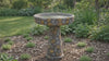 Mosaic stone concrete bird bath with colorful 
tile inlay pattern in a sunlit garden setting