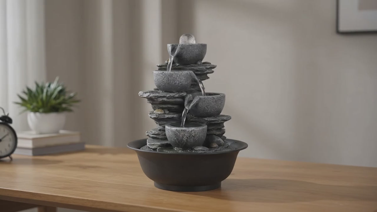 Load video: Modern tabletop water fountain with flowing water on a wooden desk bathed in natural daylight.
