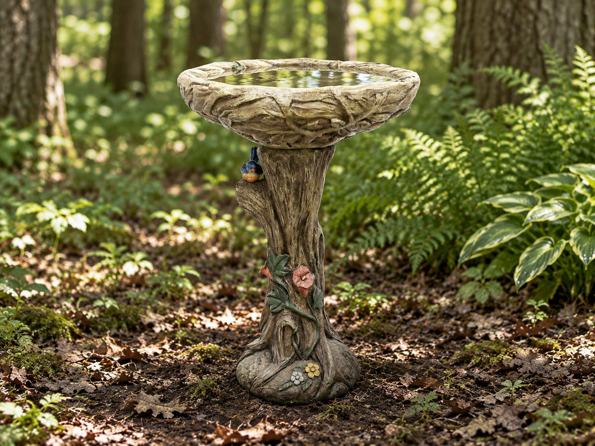 Concrete tree trunk bird bath with cast bird and blossom on a woodland floor with ferns