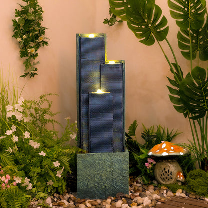 staggered dark slate column cascade fountain in a tropical garden setting with warm LED glow