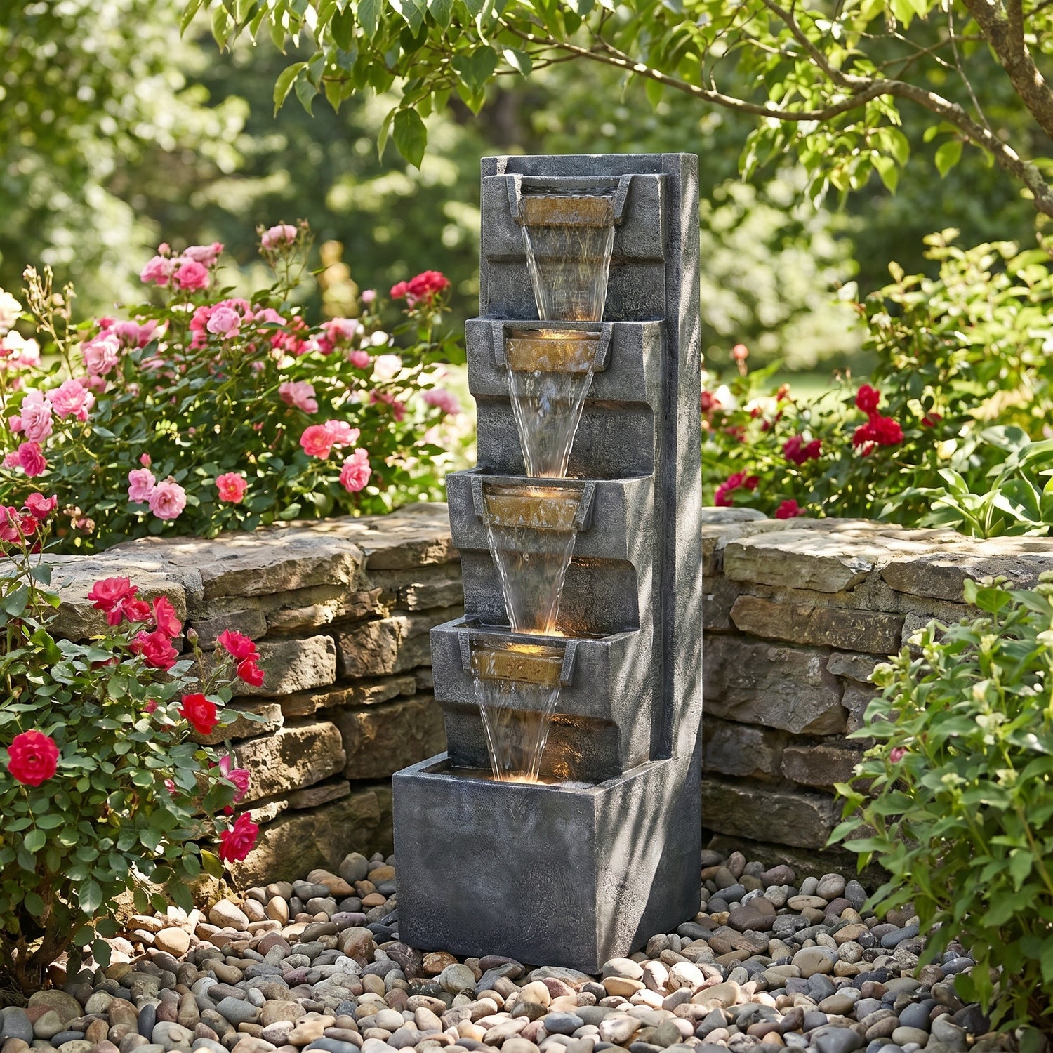 tilted basin cascade tower fountain in a garden bed with pink roses and stone wall