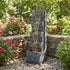 tilted basin cascade tower fountain in a garden bed with pink roses and stone wall