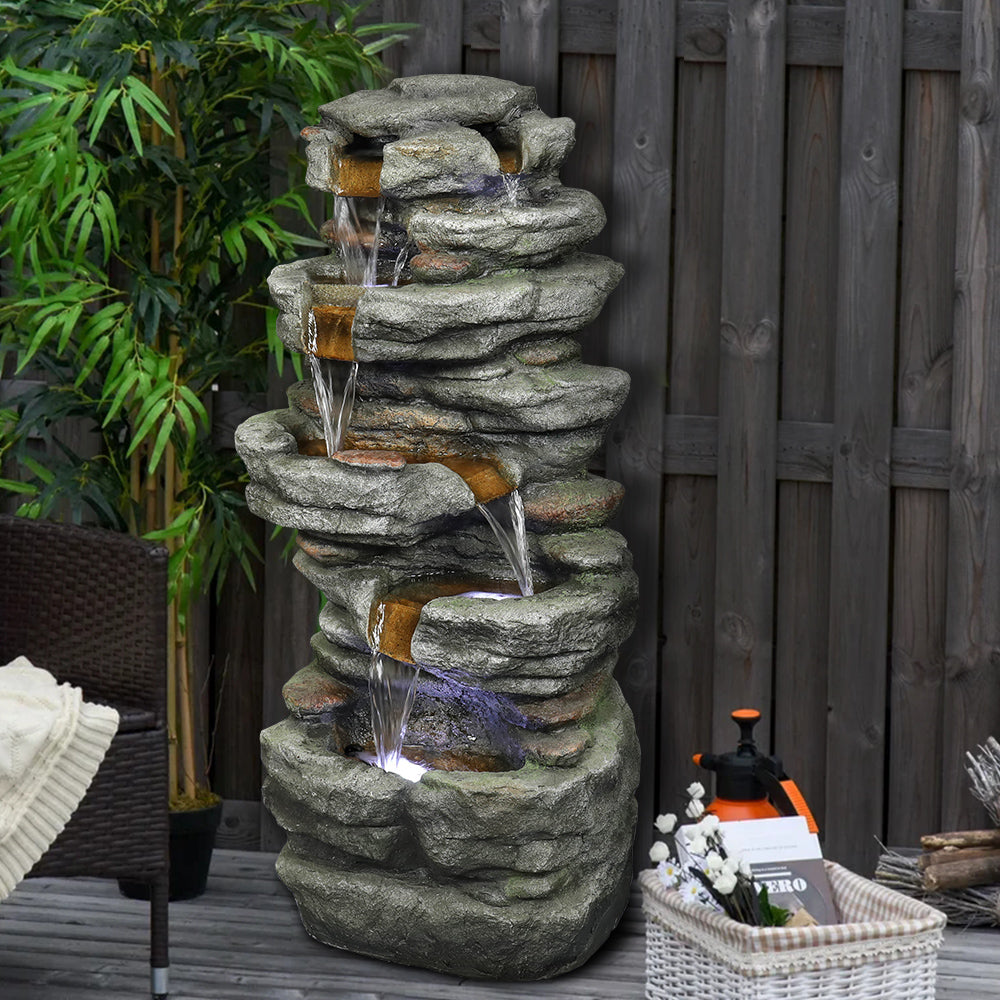 6-tier slate stone rock tower fountain tucked perfectly into a relaxing backyard fence corner.