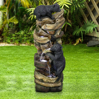 Playful bear and tree waterfall fountain standing on a green lawn in the daytime