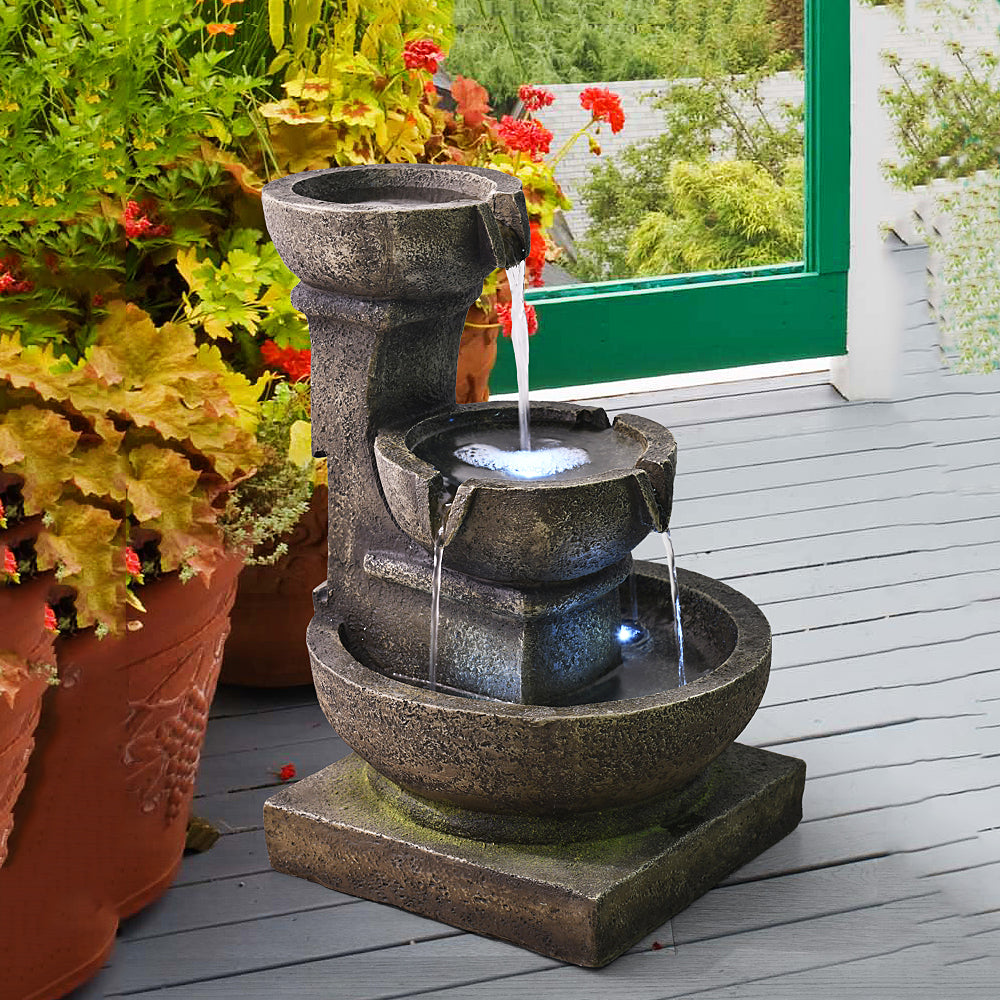 Vintage moss garden fountain positioned next to beautiful outdoor flower pots